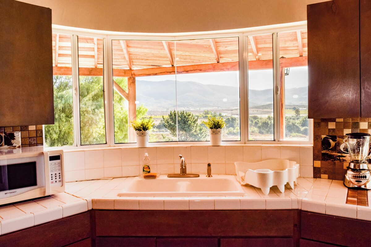 A kitchen with a large window, a sink, a microwave, and a blender.