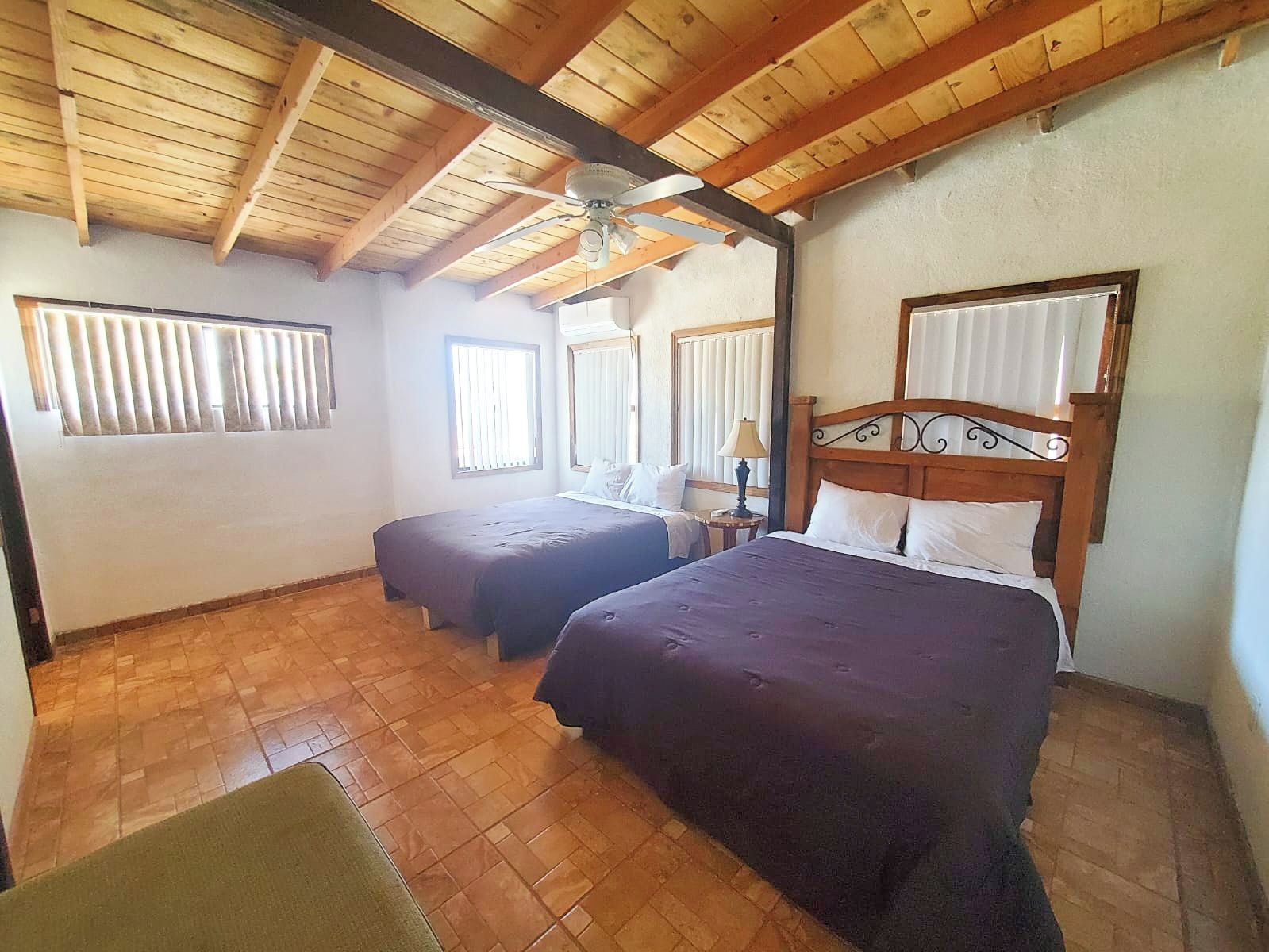 Habitación con dos camas, ventilador de techo y ventana con persianas.
