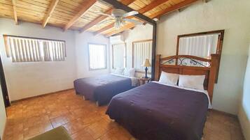 Habitación con dos camas, ventilador de techo y ventana con persianas.