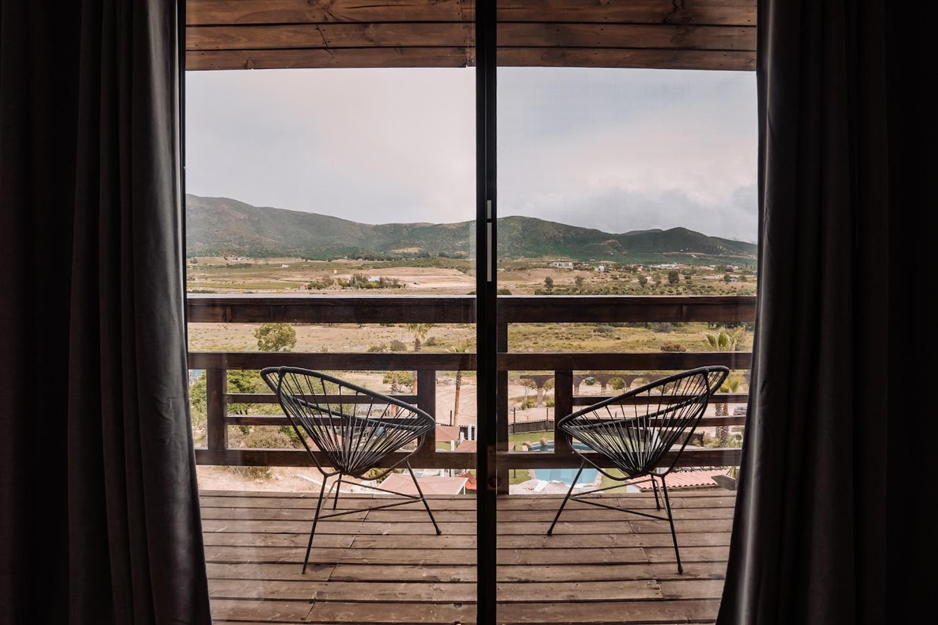 A balcony with two chairs facing a scenic view of hills and a distant village.