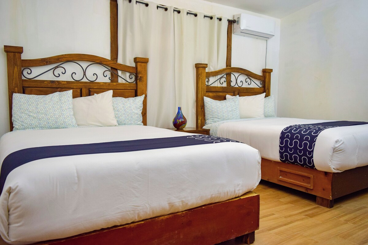 A double room with two wooden beds, white bedding, and a small vase on the nightstand.