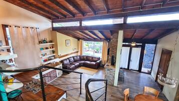A spacious living area with a wooden ceiling, a brown leather sofa, a dining table with chairs, and a staircase with a railing.