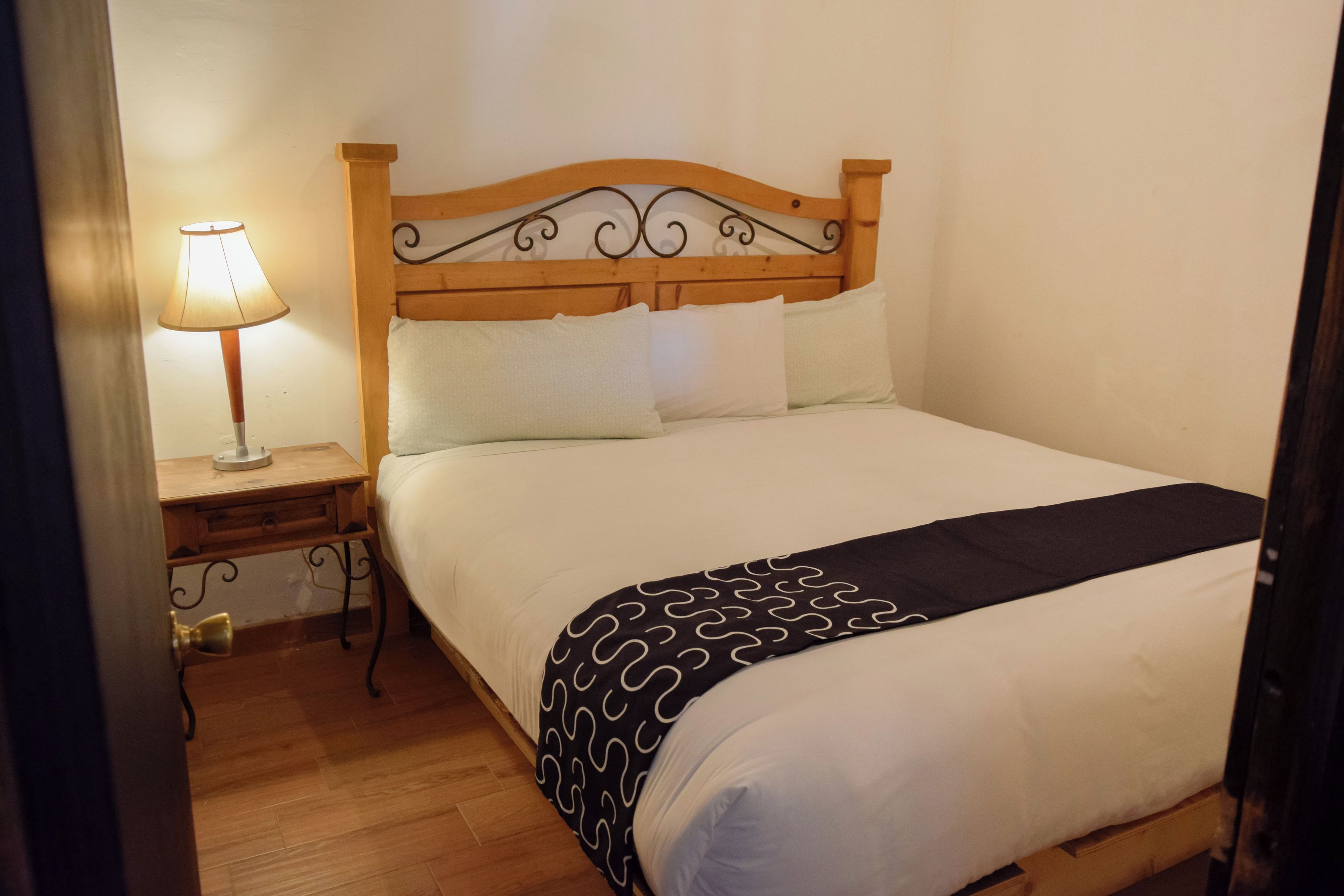 Una cama bien hecha con cabecera de madera, una mesita de noche con lámpara y una manta decorativa.