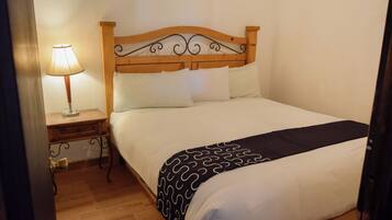 Una cama bien hecha con cabecera de madera, una mesita de noche con lámpara y una manta decorativa.