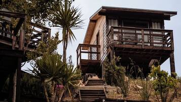 A wooden cabin with a balcony, surrounded by desert vegetation.