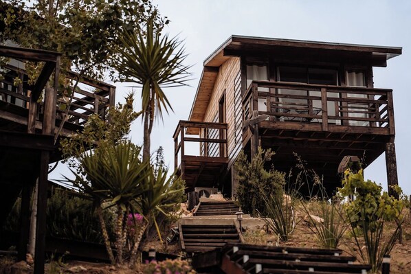 A wooden cabin with a balcony, surrounded by desert vegetation. - Finca Selah (Valle de Guadalupe)