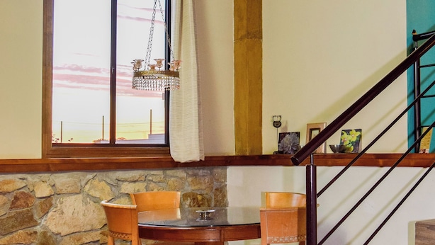 A dining area with a round table and four chairs, a stone wall, a wooden staircase, and a hanging light fixture. - Finca Selah (Valle de Guadalupe)