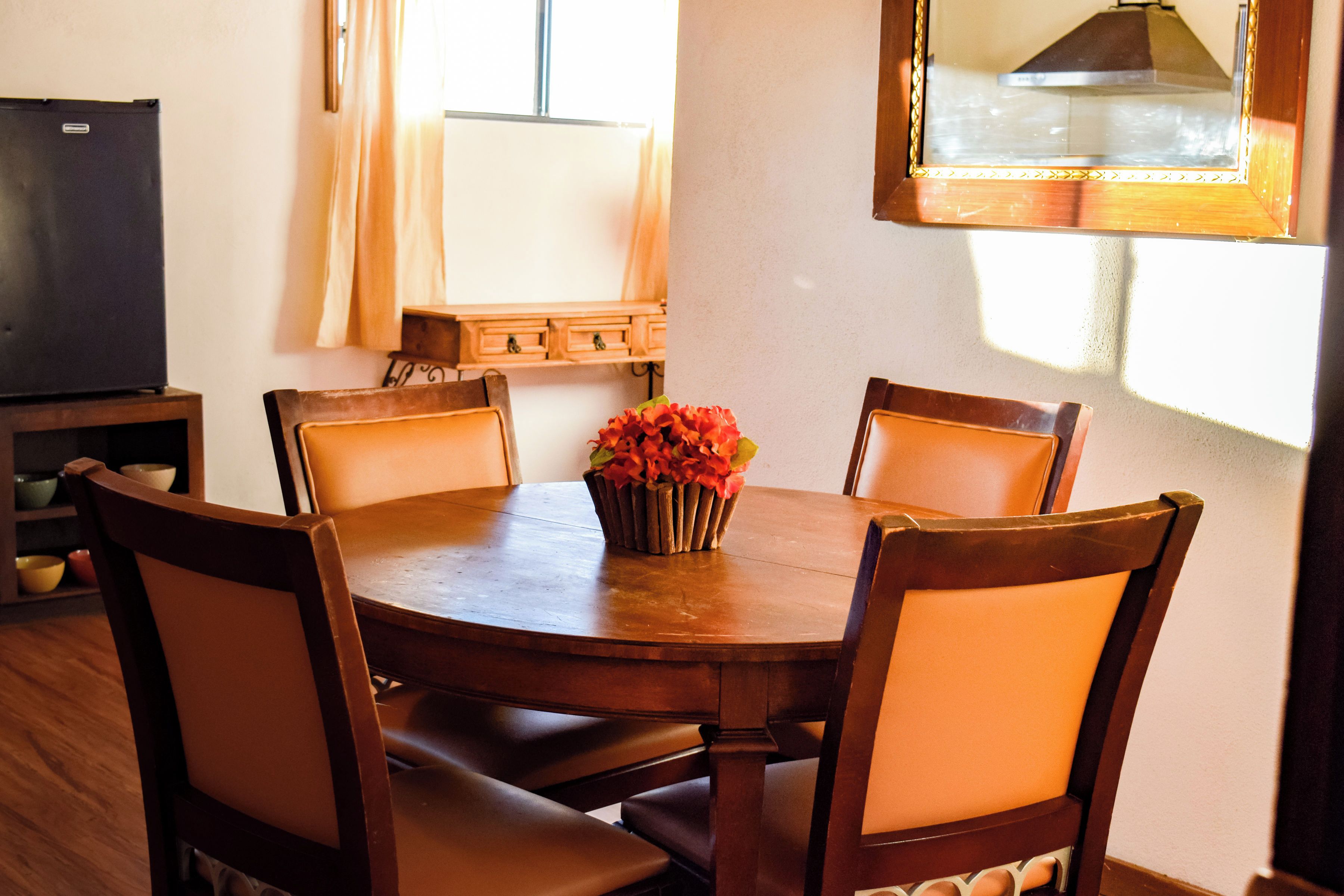 Una mesa de comedor con seis sillas, un jarrón con flores y un aparador de madera con cajones.