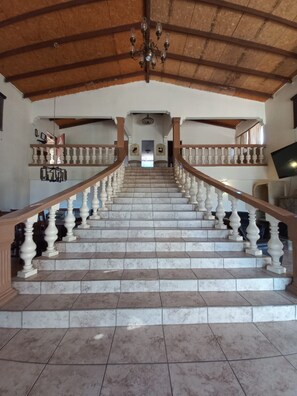 A grand staircase with marble steps and white balusters, leading to a landing with a chandelier.