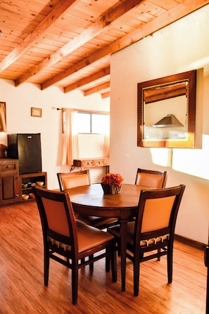 A dining area with a wooden table surrounded by chairs, a television, and a window with curtains. - Finca Selah (Valle de Guadalupe)