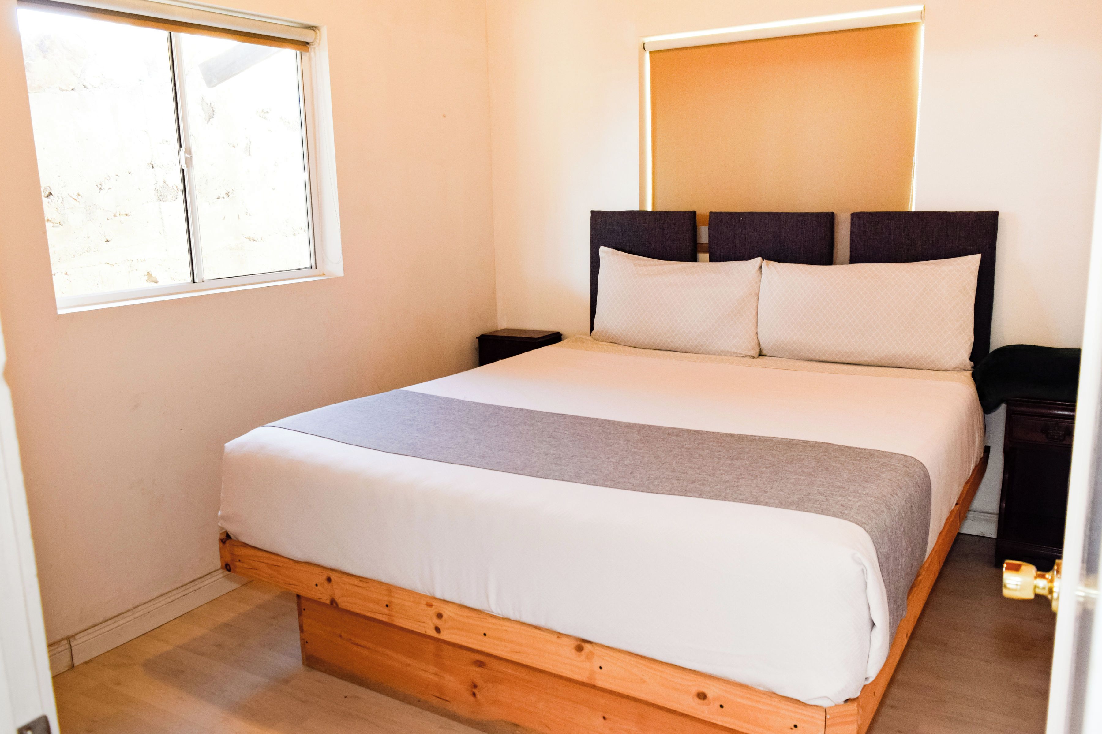 Quarto com estrutura de cama de madeira, colchão branco e cabeceira com dois travesseiros.
