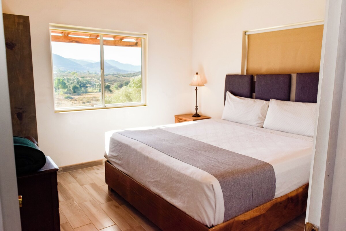 Une chambre à coucher avec un lit en bois, une table de chevet avec une lampe, une fenêtre donnant sur la campagne et une commode en bois.