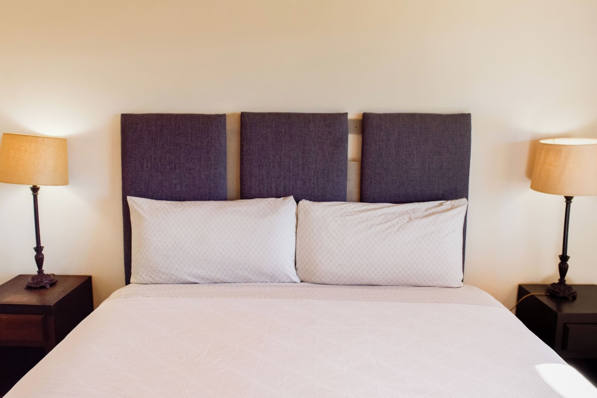 A bed with a headboard, two bedside tables, and two lamps.