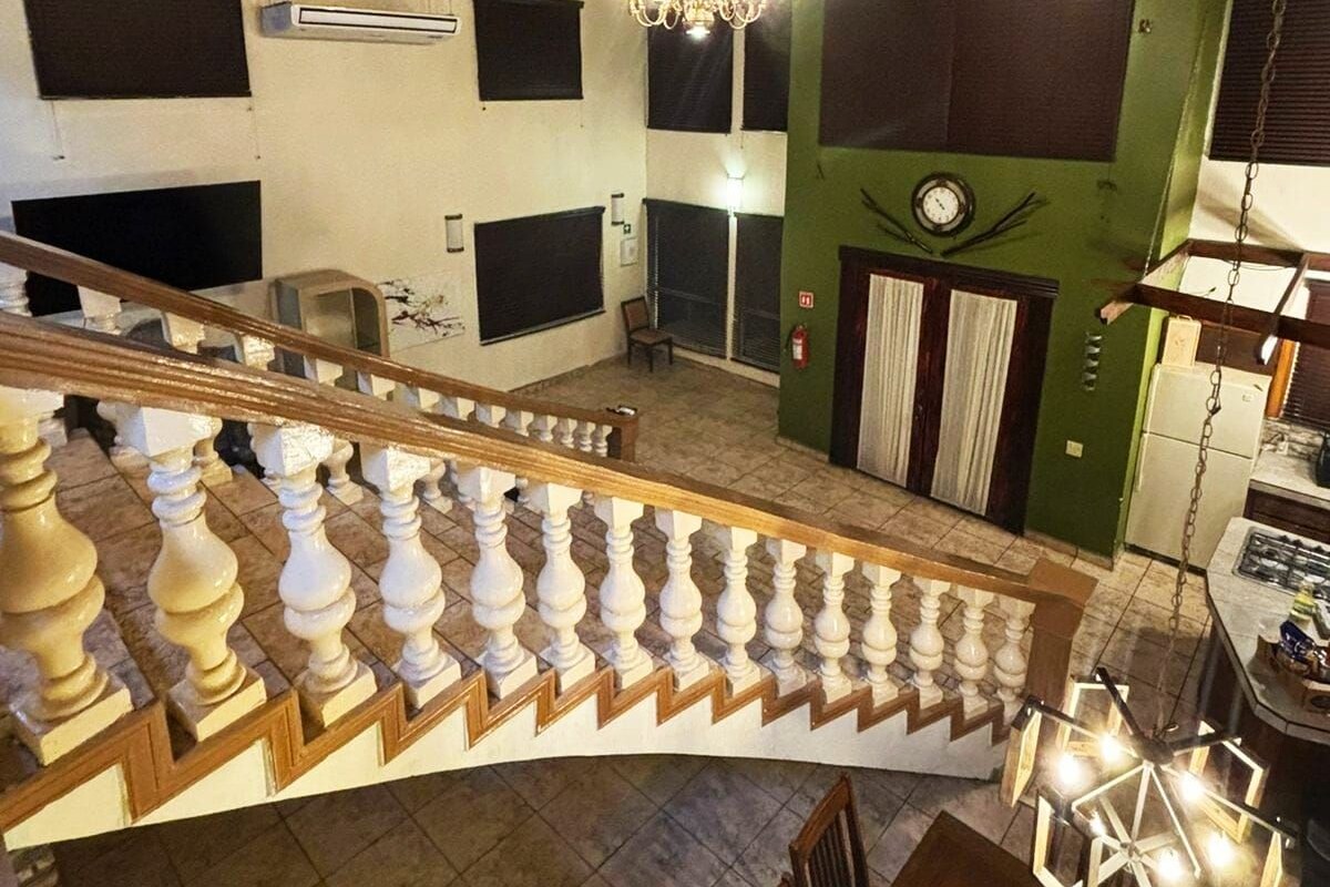 A spacious interior with a high wooden ceiling, a staircase with white balusters, and a chandelier.
