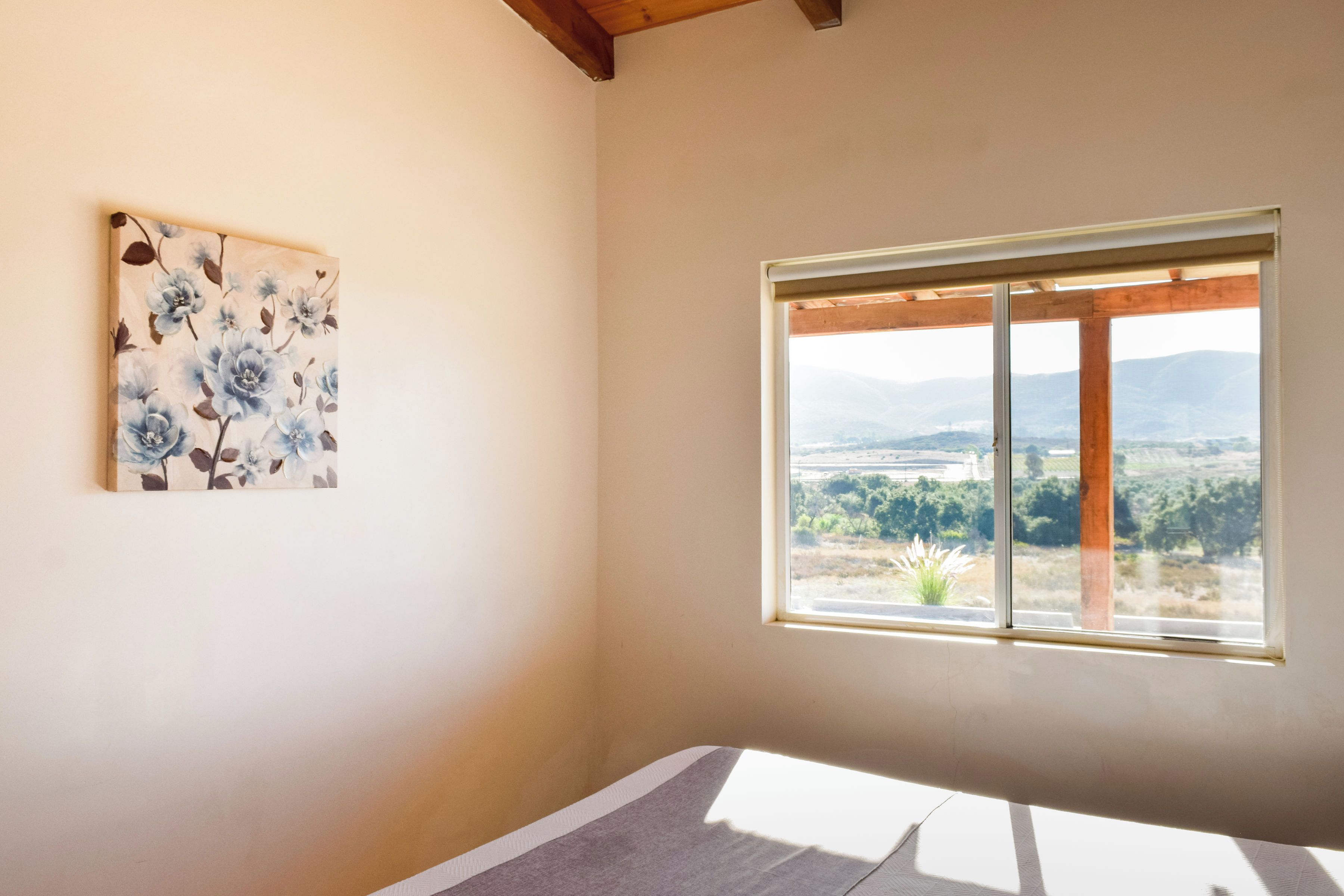 A room with a large window, a painting on the wall, and a wooden ceiling.