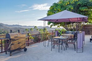 Un patio al aire libre con una parrilla, mesas, sillas y una sombrilla grande.
