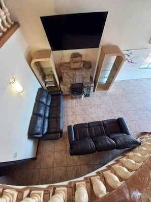 A living room with a stone fireplace, two black leather sofas, and a staircase leading to an upper level. - Finca Selah (Valle de Guadalupe)