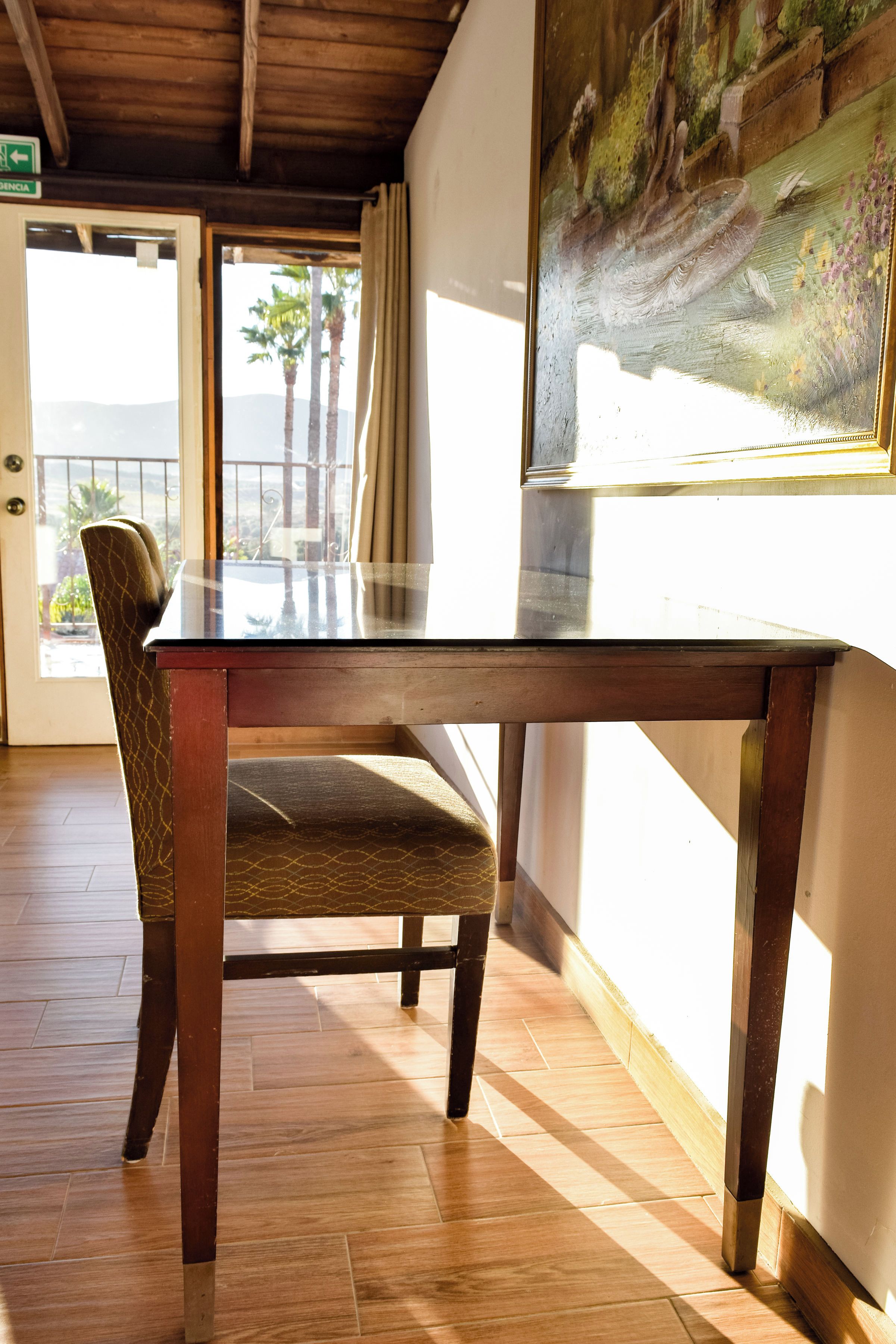 Una mesa de comedor de madera con cubierta de vidrio, una silla estampada y un cuadro en la pared.