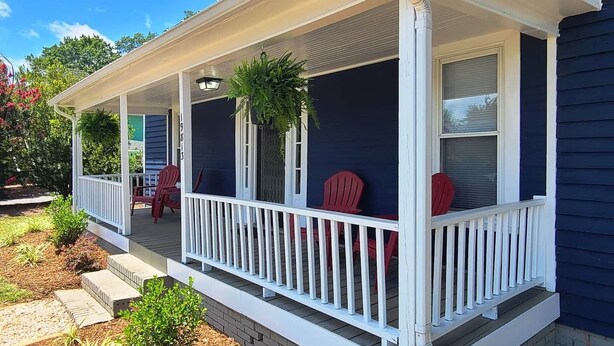 A house with a covered porch, two red Adirondack chairs, and a potted plant.