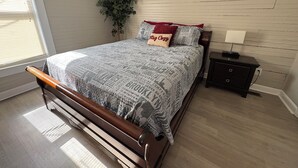 A bedroom with a wooden bed, a nightstand, a lamp, a potted plant, and a window with blinds.