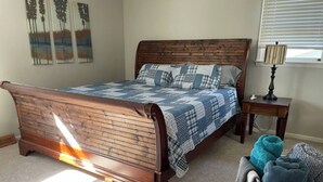 Ein Schlafzimmer mit einem Holzbett, einem Nachttisch, einer Lampe und einem Fenster mit Jalousien.