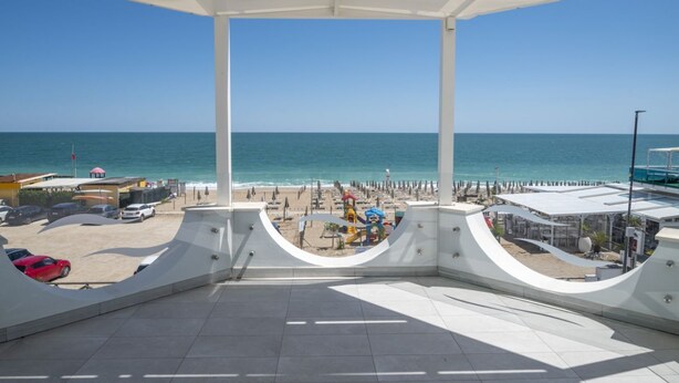 A beach view from a covered terrace with a pool, beach umbrellas, and a lifeguard tower. - M447 - Marcelli, brand new sea front three-room apartment in a residence with swimming pool (Marcelli)