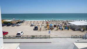 A beach view with a parking area, beach umbrellas, and a lifeguard tower. - M447 - Marcelli, brand new sea front three-room apartment in a residence with swimming pool (Marcelli)