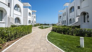 A pathway leading to a modern building with arched windows and balconies, surrounded by well-maintained grass and hedges. - M447 - Marcelli, brand new sea front three-room apartment in a residence with swimming pool (Marcelli)
