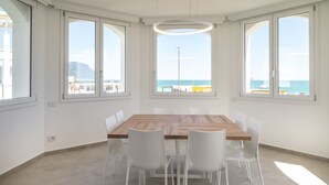 A spacious room with a large wooden table, white chairs, and large windows with a view of the sea. - M447 - Marcelli, brand new sea front three-room apartment in a residence with swimming pool (Marcelli)