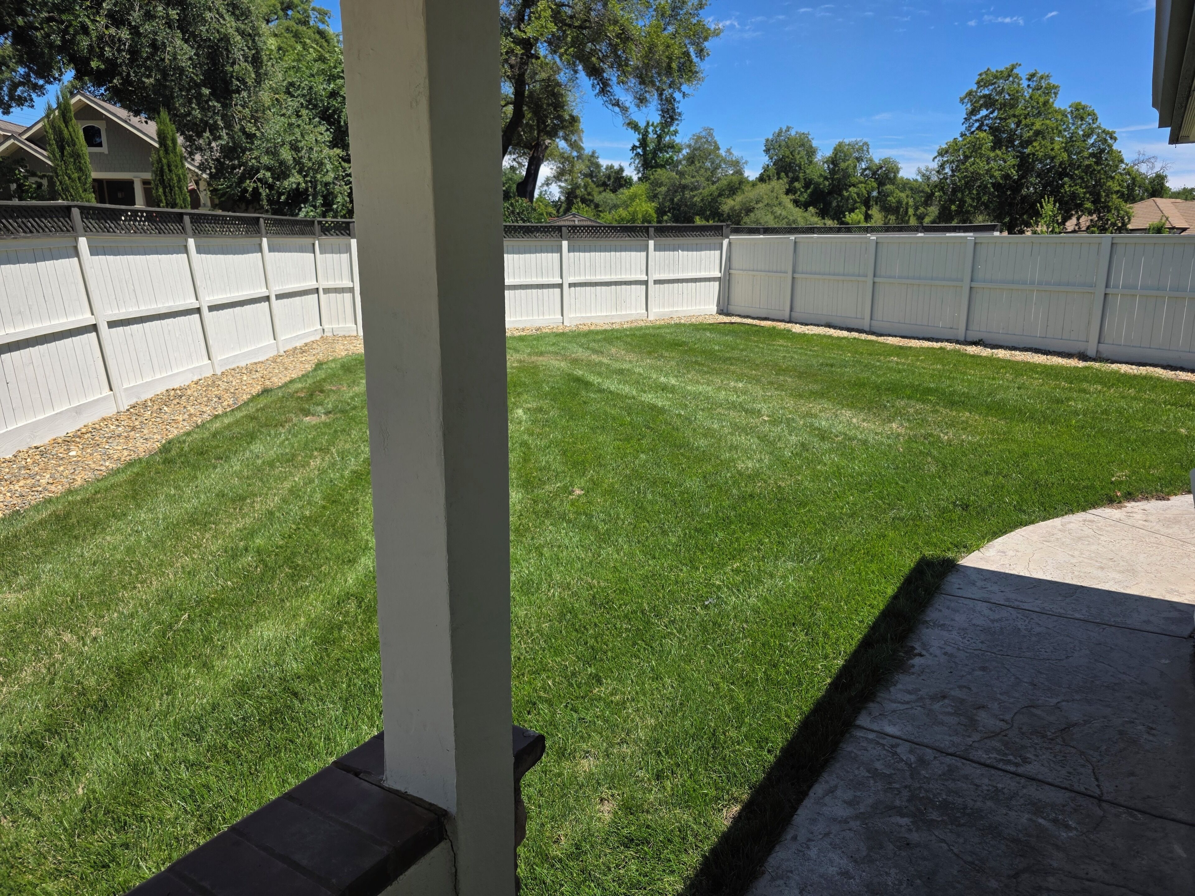 Une pelouse bien entretenue, agrémentée d’une clôture blanche et d’une terrasse en béton.