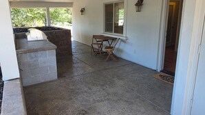 A covered patio area with a stone bench, a wooden table, and a ceiling fan.