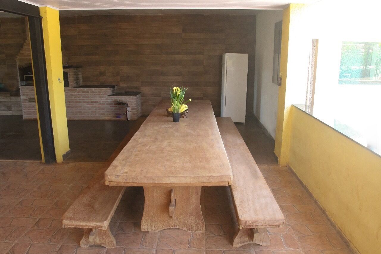 Ein langer Holztisch mit Bänken, ein Blumentopf und ein Kühlschrank in einem Raum mit Fliesenboden und Holzwänden.
