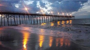 A pier extending into the ocean with lights reflecting on the water. - BEACH MUSIC - Where Every Day's a Greatest Hit (Carolina Beach)