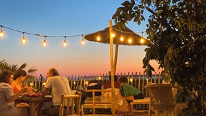 An outdoor seating area with tables and chairs, string lights, and a thatched umbrella.