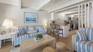 A spacious living area with a striped sofa, a coffee table, and a dining area with chairs. A kitchen is visible in the background. - 5BR/4BA-Oceanview-Pool-Sundeck-Bike-Theater-Game Room-Sleep 16+ (Ocean City)