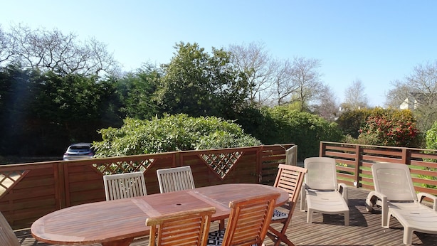 Eine Terrasse im Freien mit Holztisch und -stühlen, umgeben von einem Holzzaun und Grünpflanzen.