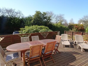Eine Terrasse im Freien mit Holztisch und -stühlen, umgeben von einem Holzzaun und Grünpflanzen.