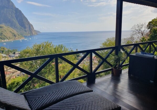 Un balcon offrant une vue sur l’océan et les montagnes, agrémenté de meubles en osier et d’une plante en pot.