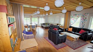 A spacious living area with a wooden ceiling, black leather sofas, a wooden coffee table, and a bookshelf filled with books. - Ansgarsgården (Flen)