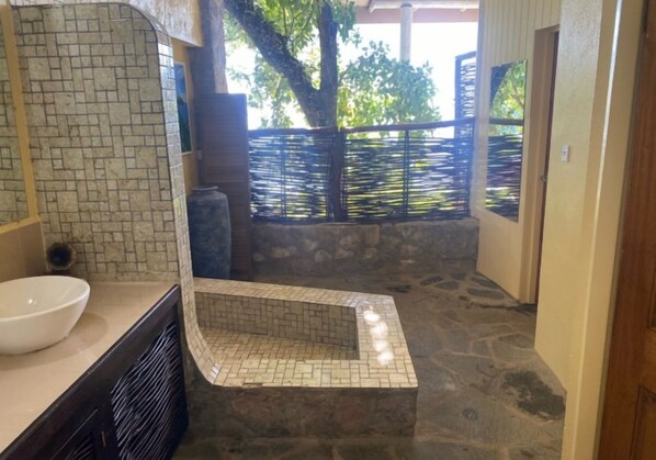 A bathroom with a stone floor, a white sink, and a tiled shower area.