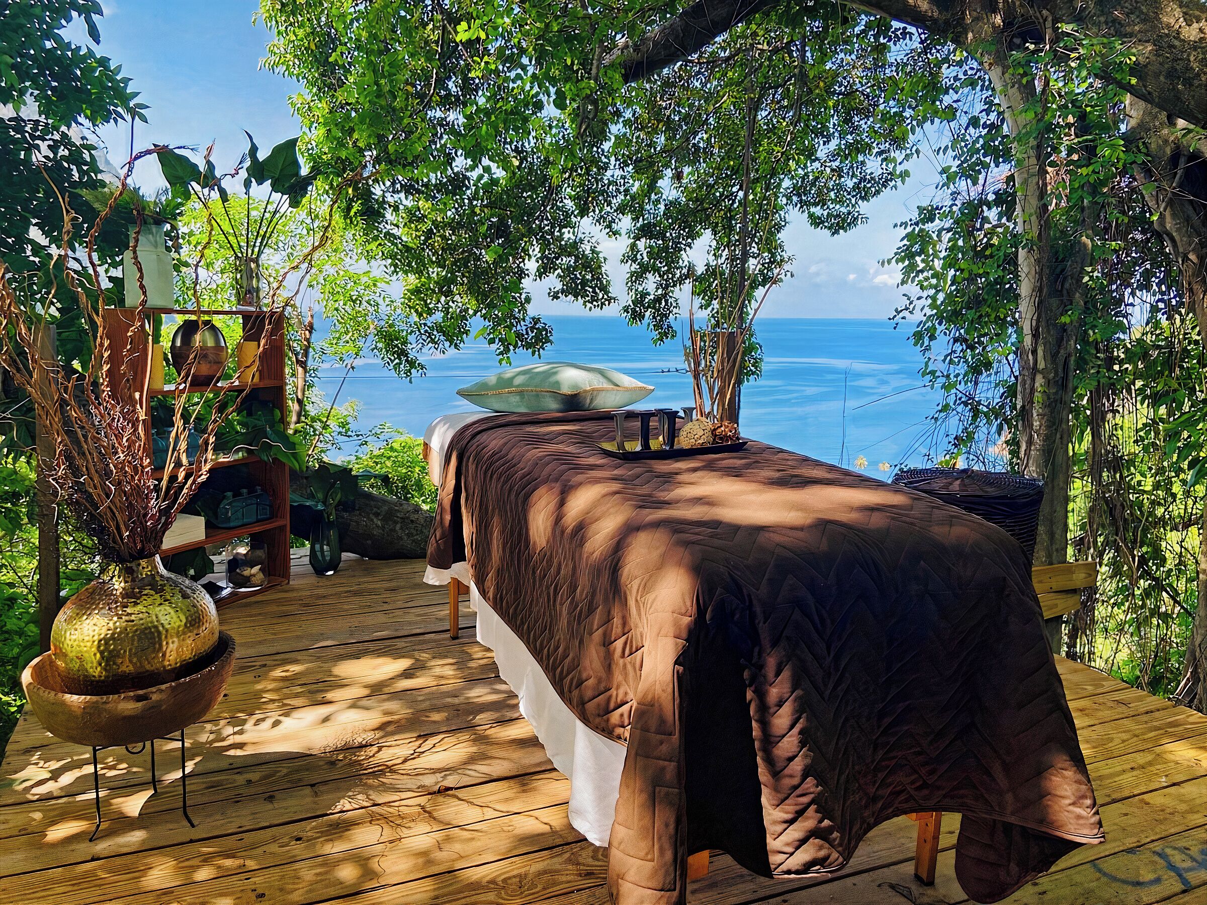 A wooden deck with a massage table, surrounded by greenery and overlooking a body of water.