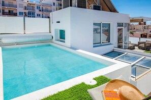 Ein moderner Poolbereich im Freien mit einer gläsernen Terrasse, einer kleinen Sitzecke und einem Buch mit dem Titel "Spanish and Portuguese Short Stories".