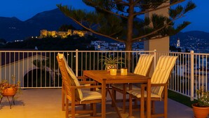 A wooden table with chairs and a potted plant on a balcony with a view of a city and mountains in the background. - Kalamata Cozy Nest With Panoramic Views (Kalamata)