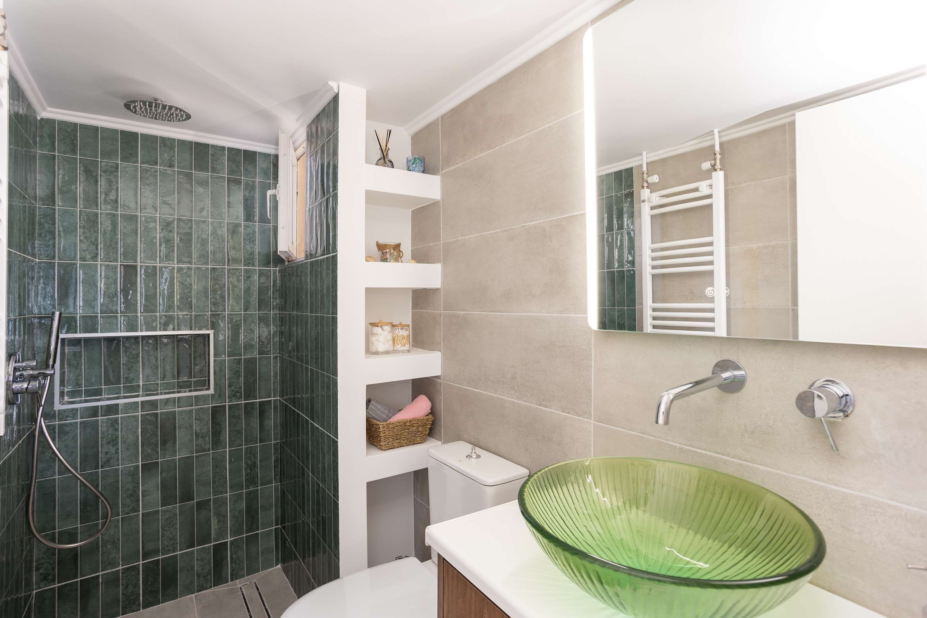 A modern bathroom with a green glass sink, a shower with a glass door, and a white vanity.