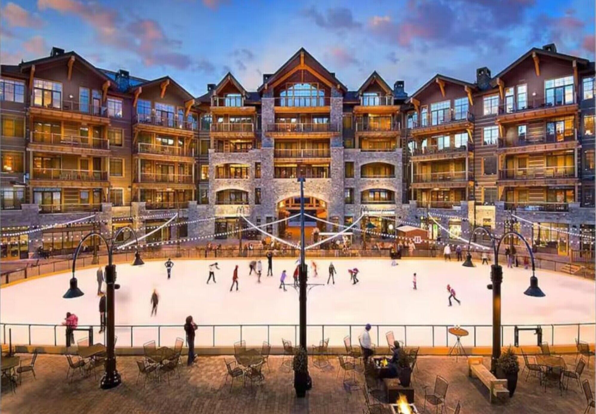 A multi-story hotel with a central ice rink, outdoor seating, and a mountainous backdrop.