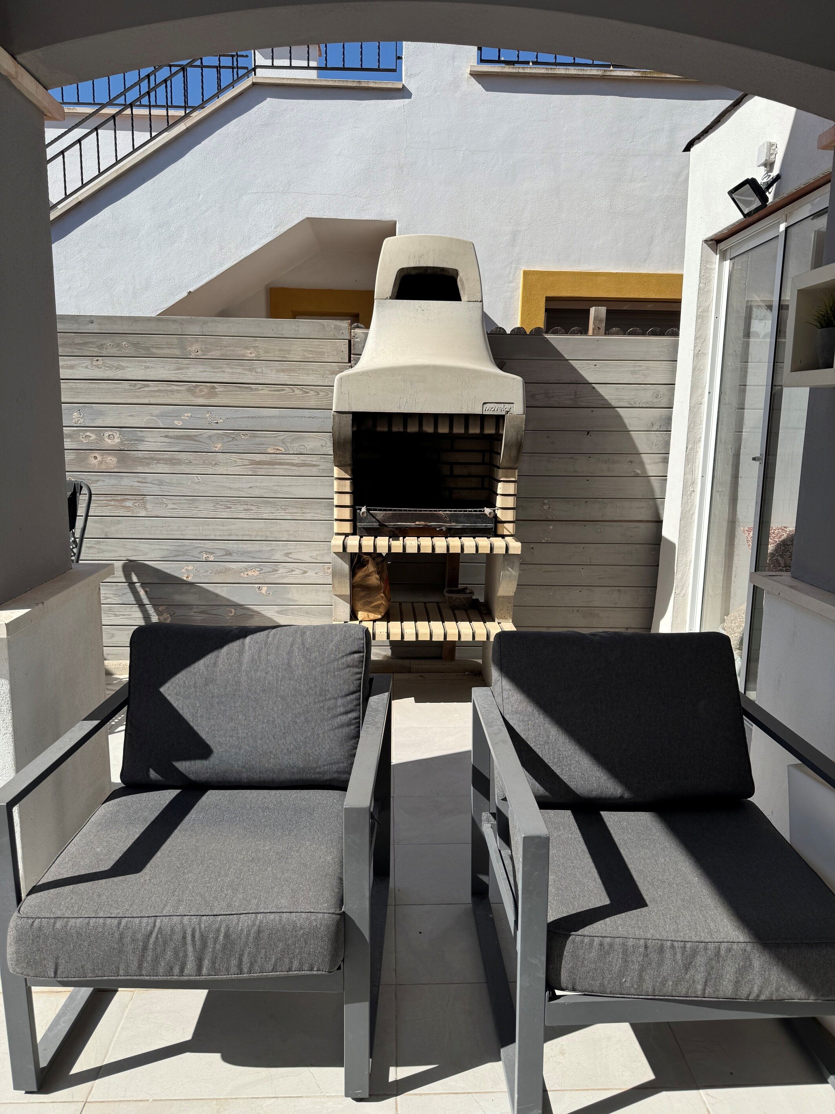 Ein Balkon mit zwei grauen Sitzgelegenheiten, einem Holzofen für Pizza und Blick zum Himmel.