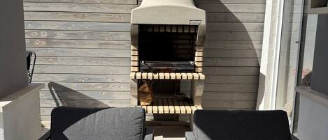 Ein Balkon mit zwei grauen Sitzgelegenheiten, einem Holzofen für Pizza und Blick zum Himmel.