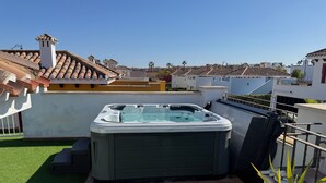 A rooftop with a hot tub, artificial grass, and a view of neighboring buildings.