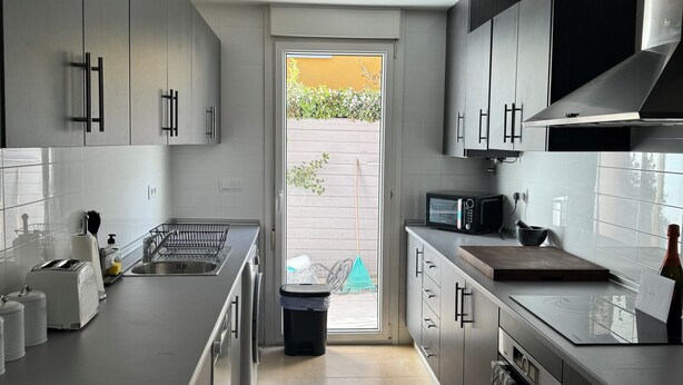 A modern kitchen with grey cabinets, a large island, and a view to the outside.