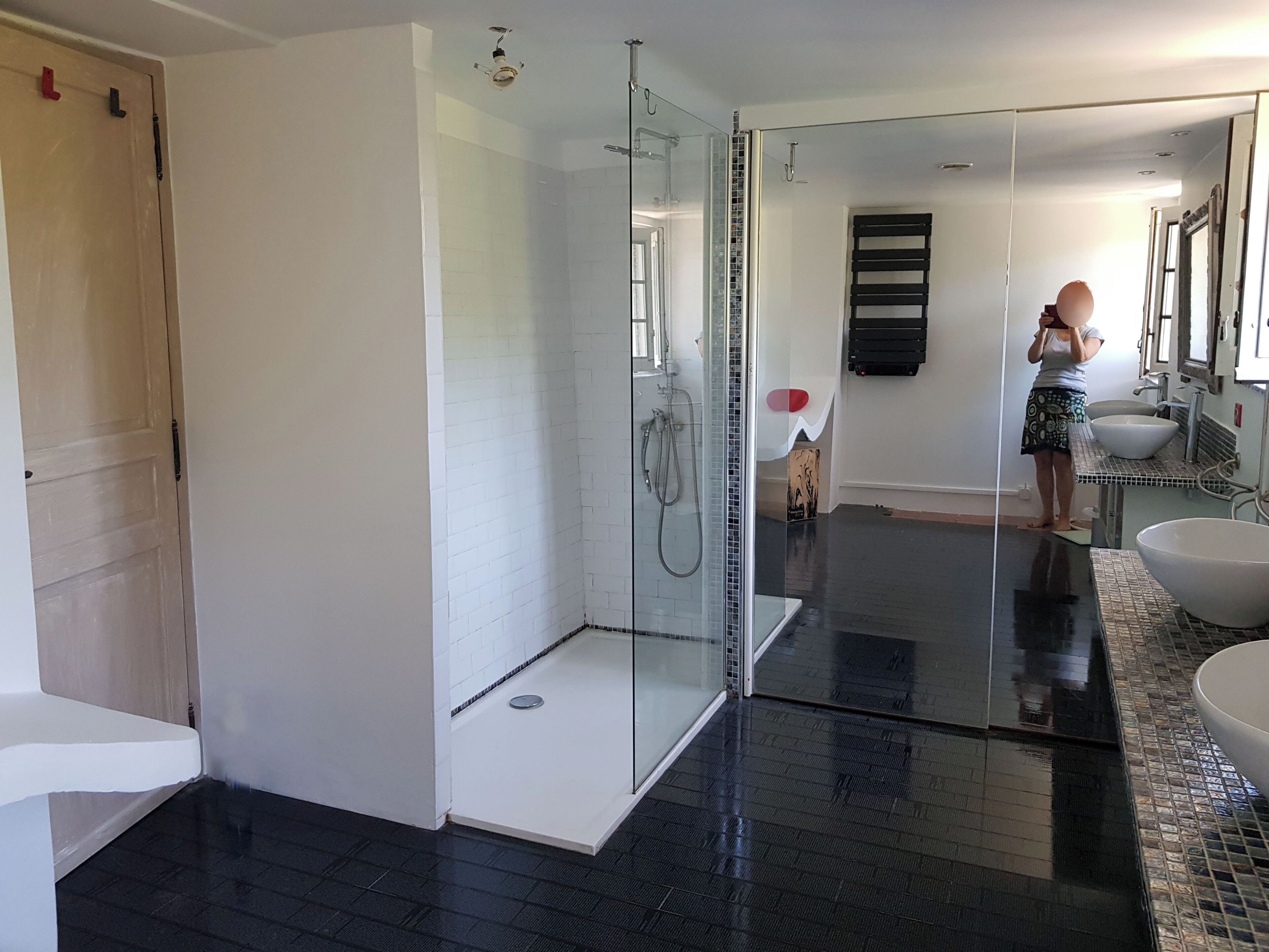 Een moderne badkamer met een douchecabine van glas, een grote spiegel en een wastafel met een witte wasbak.